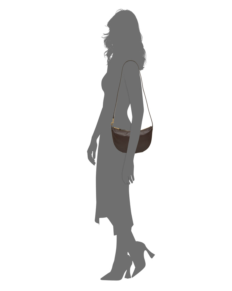 A silhouette of a woman in a dress and heels stands holding the Vince Camuto Orlie Crossbody Bag. The stylish Orlie Crossbody Bag by Vince Camuto stands out against the crisp white background.