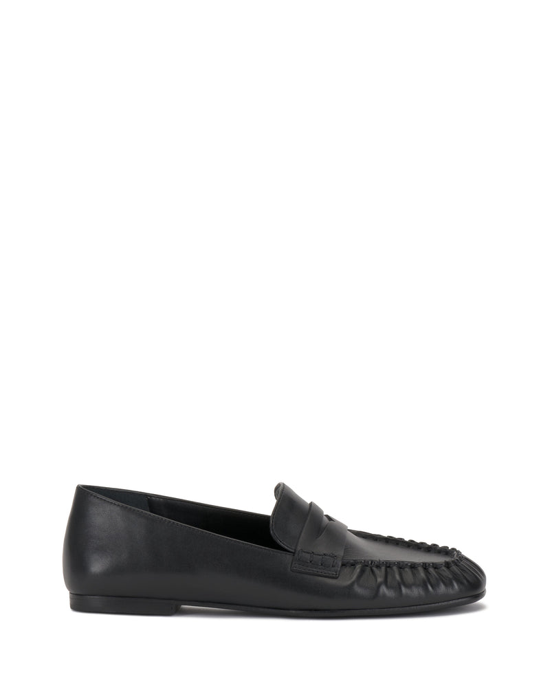 The Vince Camuto Paelyn Penny Loafer is a black leather slip-on with a moccasin-style toe, low heel, and classic penny slot detail, shown in profile against a white background.