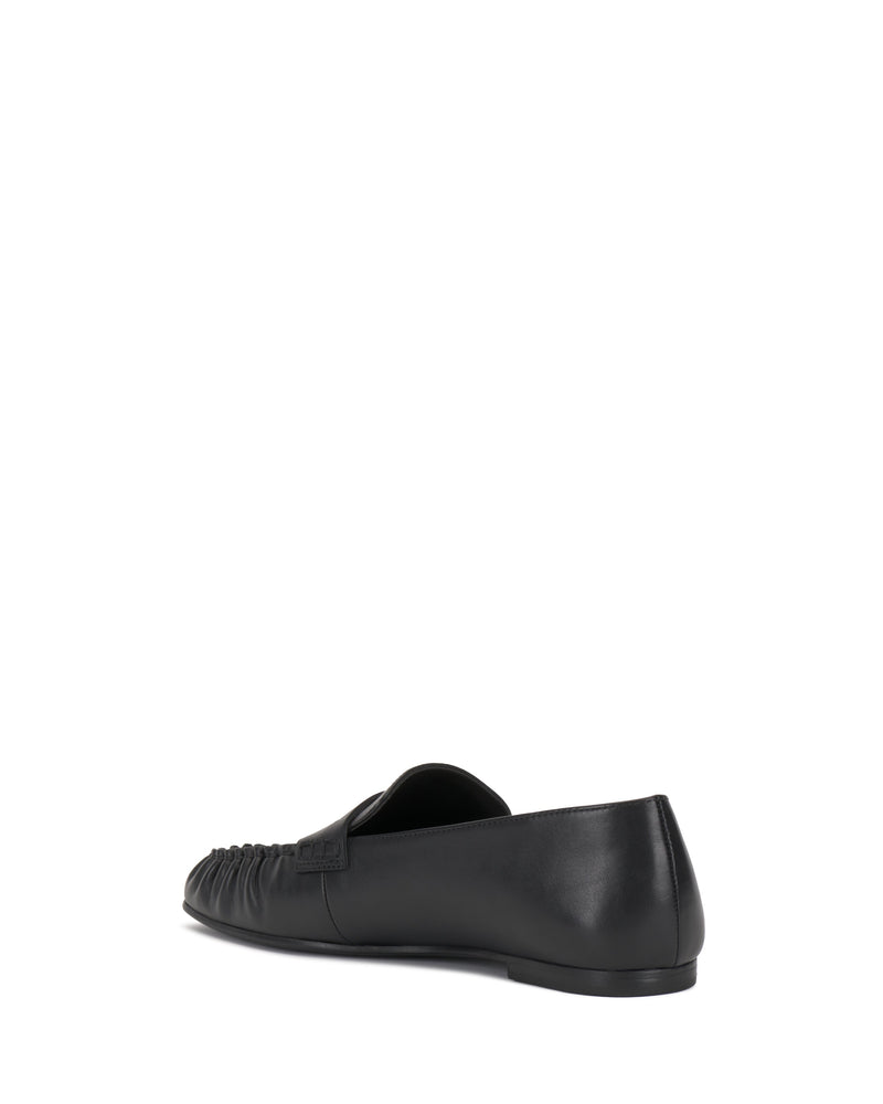The Vince Camuto Paelyn Penny Loafer, a single black leather shoe with moccasin-inspired design, low heel, gathered toe detail, and smooth finish, is shown from the rear side against a white background.