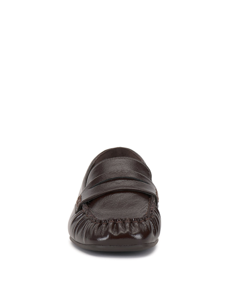 A front-facing view of the Vince Camuto Paelyn Penny Loafer in dark brown leather showcases its moccasin-style toe and top strap. This classic slip-on is displayed against a white background.