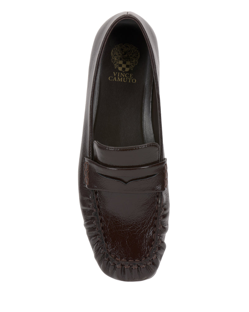 A top view of the Paelyn Penny Loafer by Vince Camuto shows a dark brown leather slip-on with a stitched moc toe, penny slot on the vamp, and a black insole featuring the gold Vince Camuto logo.