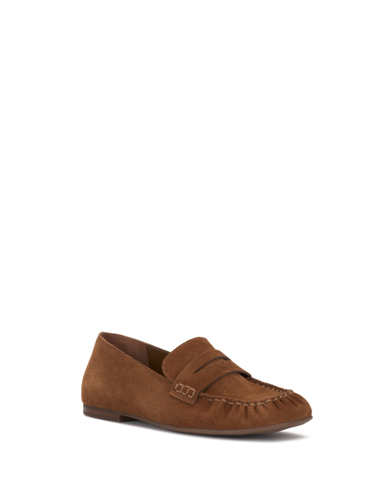 The Vince Camuto Paelyn Penny Loafer features brown suede, moccasin-style stitching, a low heel, and a decorative strap across the top, shown against a plain white background.
