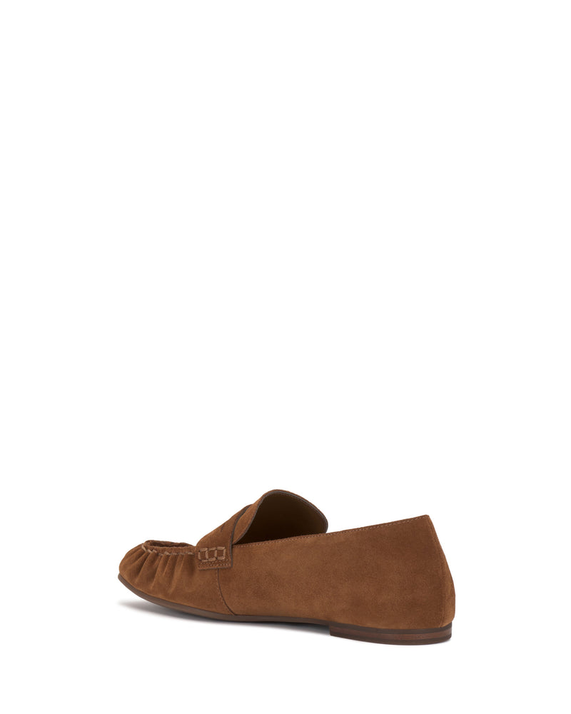 The Vince Camuto Paelyn Penny Loafer is a brown suede flat with ruched detailing, a small buckle accent, and moccasin-inspired design, displayed from a rear side angle on a white background.