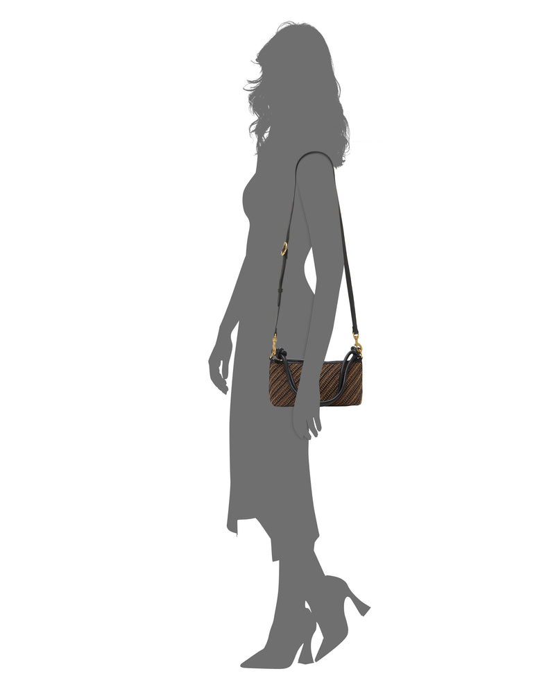 A woman in a mid-length dress and heels carries the Vince Camuto Paula Crossbody Bag—small, brown with a black strap and gold hardware—against a plain white background.