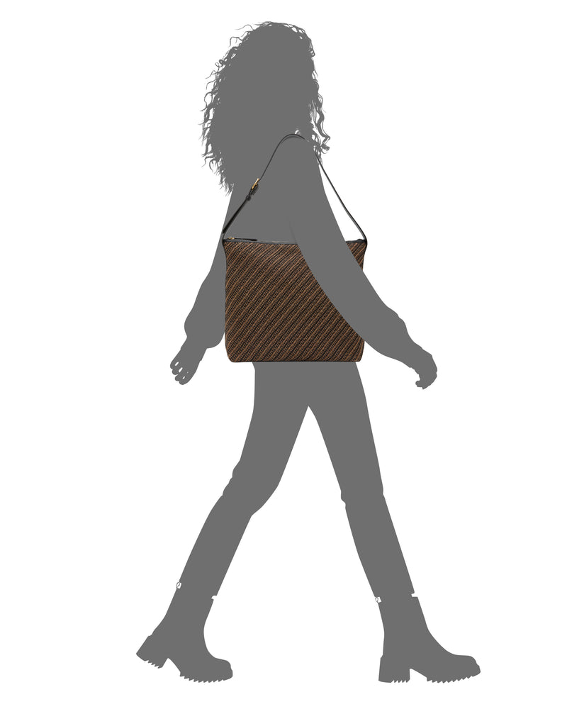 A person with curly hair walks, wearing boots and pants and carrying the Vince Camuto Paula Shoulder Bag—brown with stripes—against a white background.