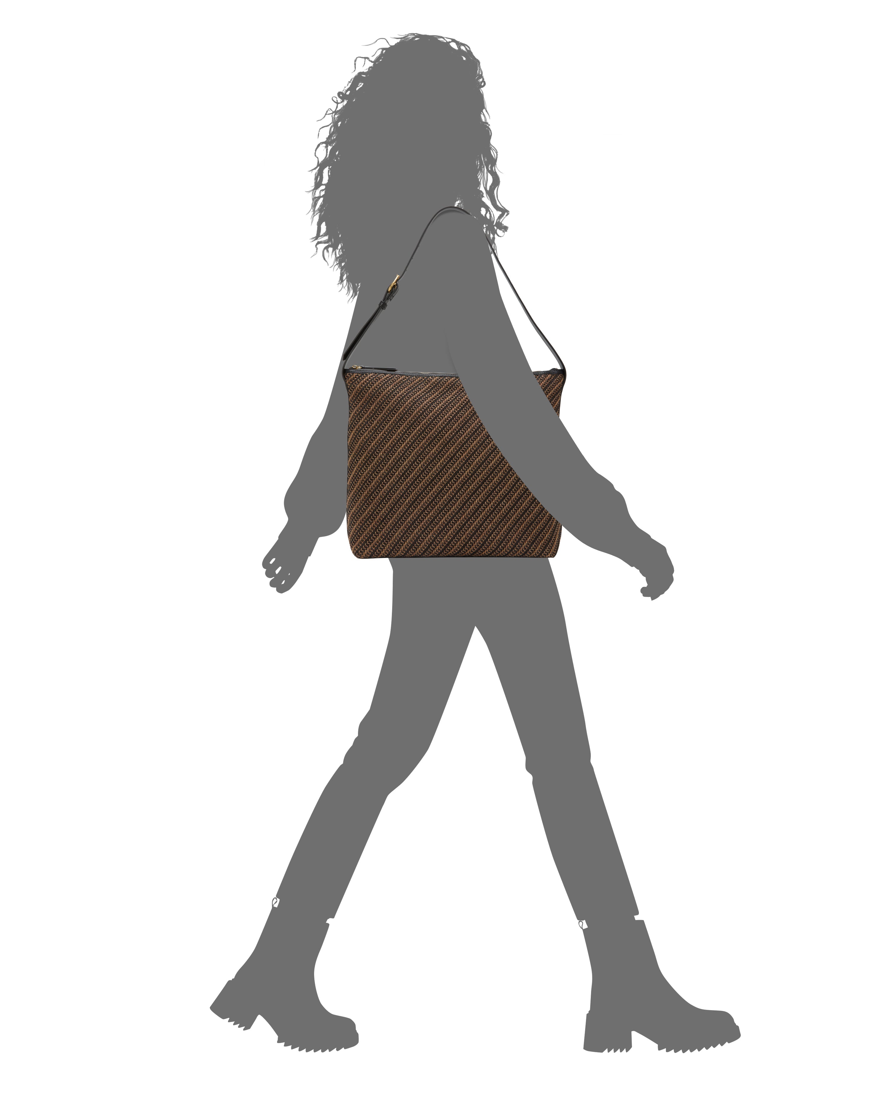 Silhouette of a person with curly hair walking in boots, carrying the Vince Camuto Paula Shoulder Bag—a brown striped canvas style—over their shoulder against a white background.