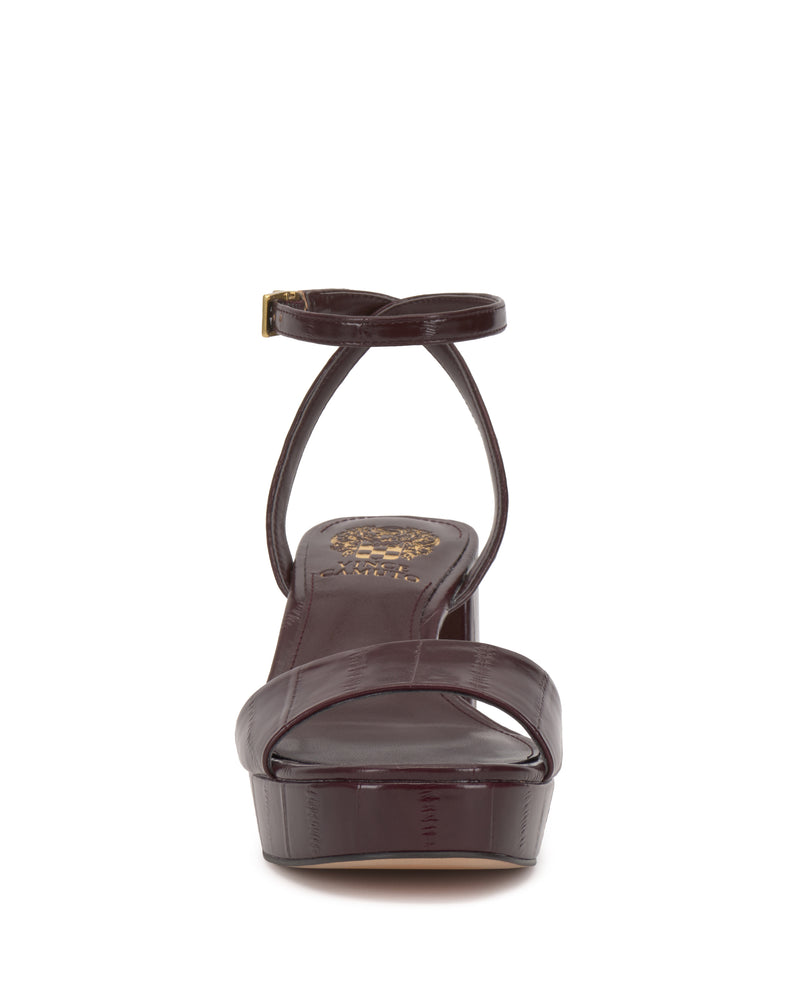 Front view of the Vince Camuto Pendreya Platform Sandal in dark brown, featuring an open toe, block heel, crisscross toe strap, ankle strap with small buckle, and a gold decorative logo on the insole for retro charm.