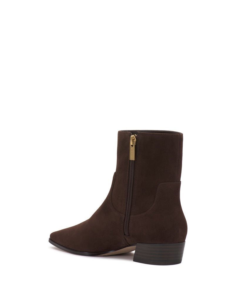 The Pertula Bootie by Vince Camuto is a dark brown suede ankle boot with a low block heel, pointed toe, and gold side zipper, shown against a white background.