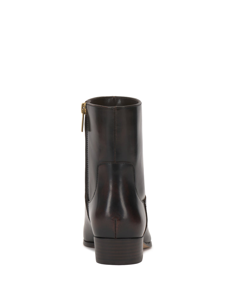 The Vince Camuto Pertula Bootie is shown from the back in dark brown leather, featuring a polished finish, visible stitching, a low stacked heel, and a convenient side zipper with a gold pull tab that highlights its classic style.