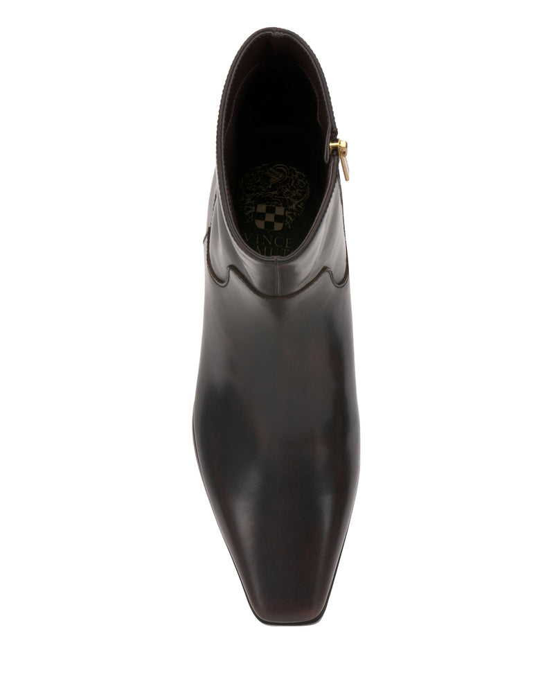 Top view of a single Vince Camuto Pertula Bootie in dark brown leather, showcasing a pointed toe ankle bootie silhouette with stitched detailing near the ankle and a small gold side zipper. The interior features an elegant decorative gold pattern, completing this chic block heel bootie.