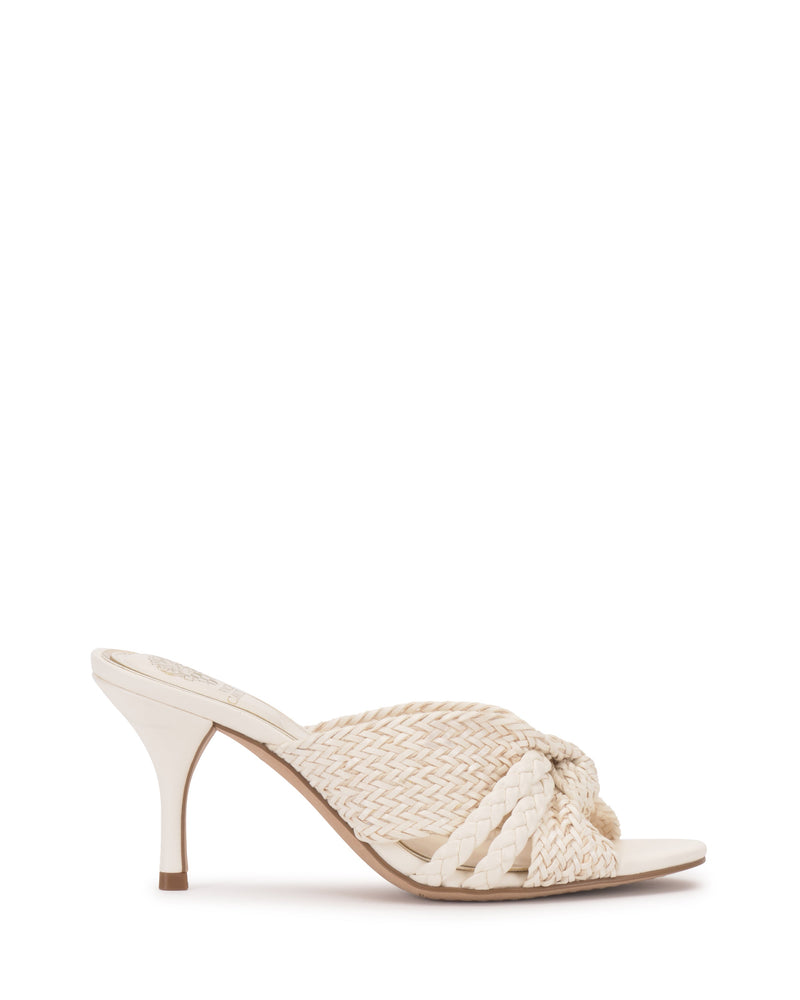 The Vince Camuto Pheya Mule is an ivory heeled sandal with a woven braided crisscross strap, open toe, and mid-height stiletto heel, displayed against a plain white background.