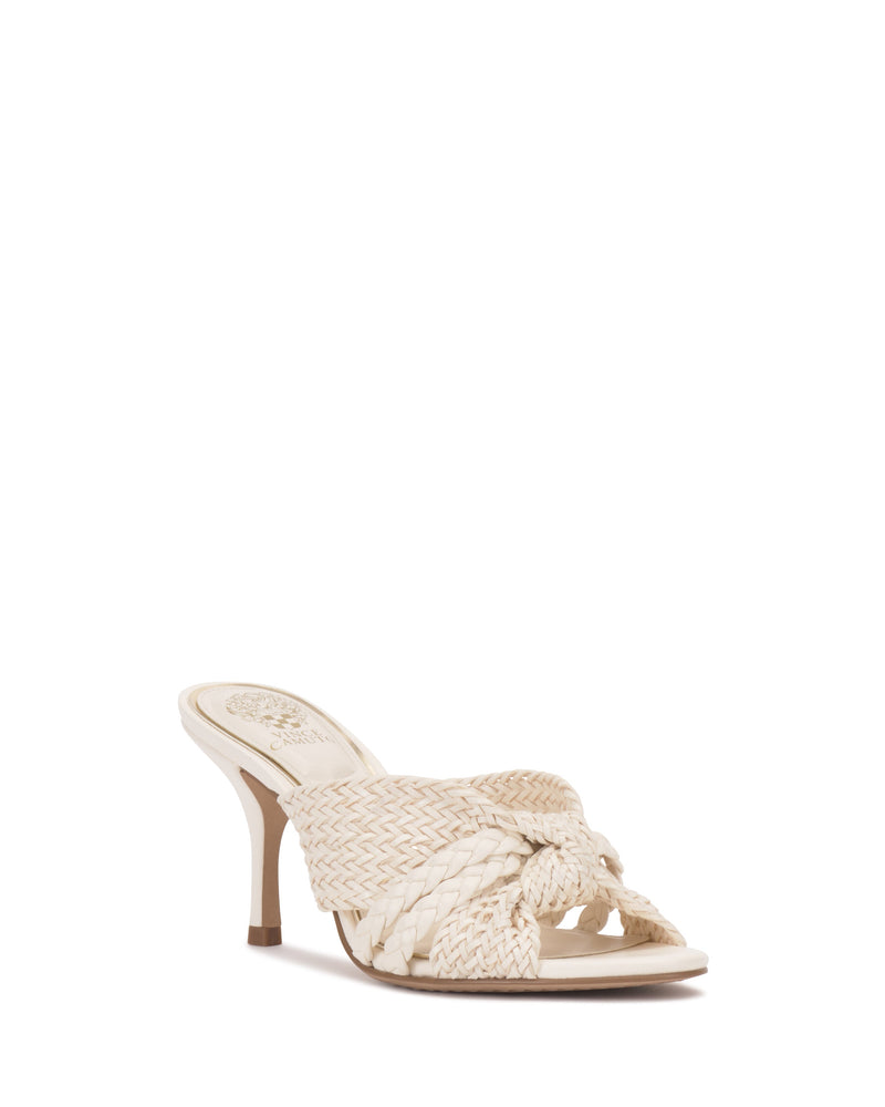 The Vince Camuto Pheya Mule is a beige heeled sandal with a woven, braided upper featuring a knotted detail, open toe, and medium stiletto heel, displayed against a white background.