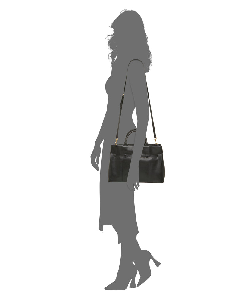 The Rilah Satchel Bag by Vince Camuto, featuring black leather and gold hardware, is displayed on the shoulder of a female silhouette in profile, dressed in a midi dress and high heels.
