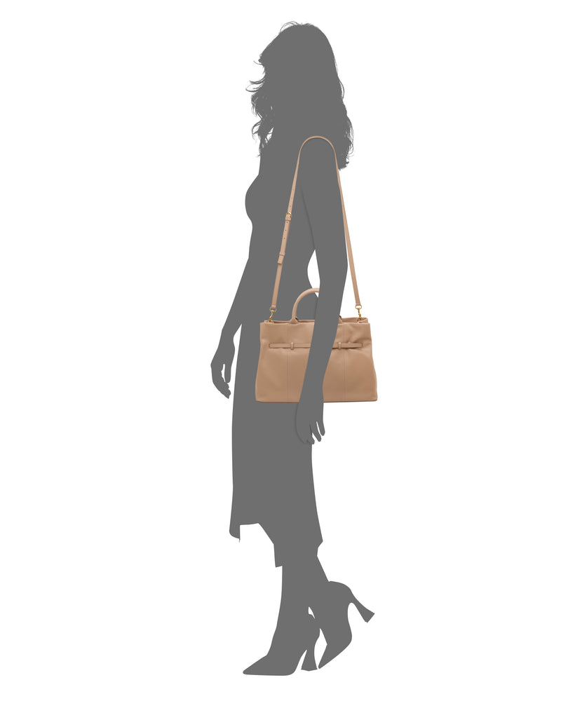Silhouette of a woman in profile, wearing heeled shoes and a midi dress, carrying the Vince Camuto Rilah Satchel Bag—a tan leather shoulder bag with a top handle and gold hardware.