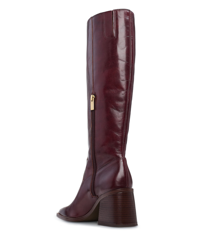 The Sangeti Boot by Vince Camuto is a tall, burgundy leather boot with a shiny finish, square toe, stacked block heel, and side gold zipper pull, shown from the back at an angle.