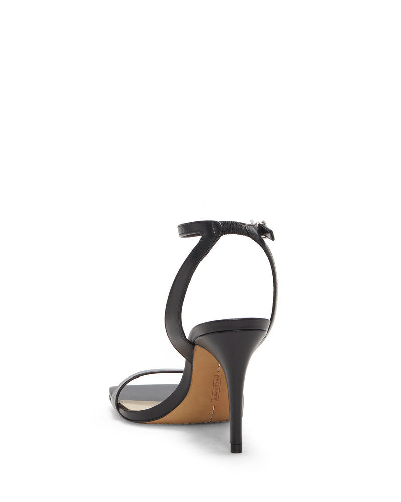 The Vince Camuto Saprenda Sandal is a black heeled sandal with a thin ankle strap and buckle, low tapered heel, light-colored insole, and tan outsole, viewed from the back.