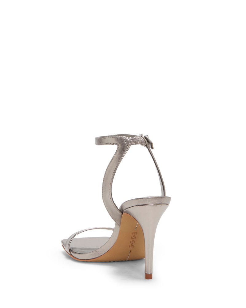 The Vince Camuto Saprenda Sandal is shown from the rear angle on a white background, crafted from metallic silver leather with an elegant ankle strap and a back zipper.