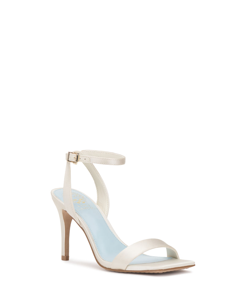 The Saprenda Sandal by Vince Camuto features a white metallic leather design with an ankle strap, gold buckle, open toe, and light blue insole, shown on a white background.