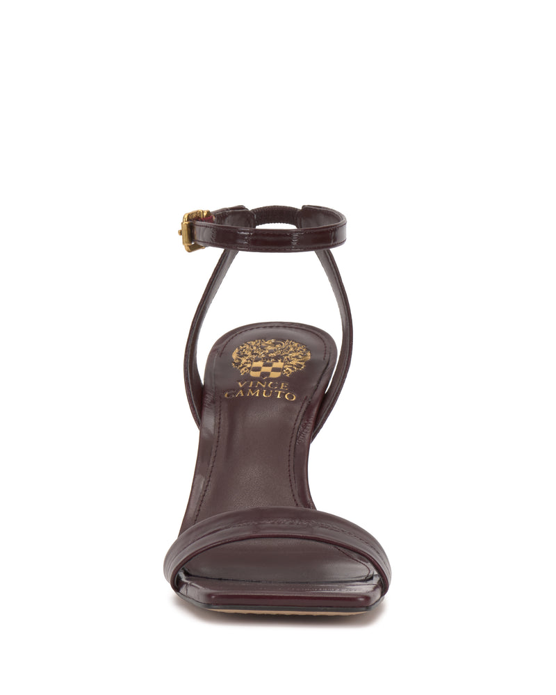 Front view of the Vince Camuto Saprenda Sandal in dark burgundy metallic leather, featuring an open toe, single toe strap, slim ankle strap with gold buckle, and gold Vince Camuto logo on the insole, displayed on a white background.