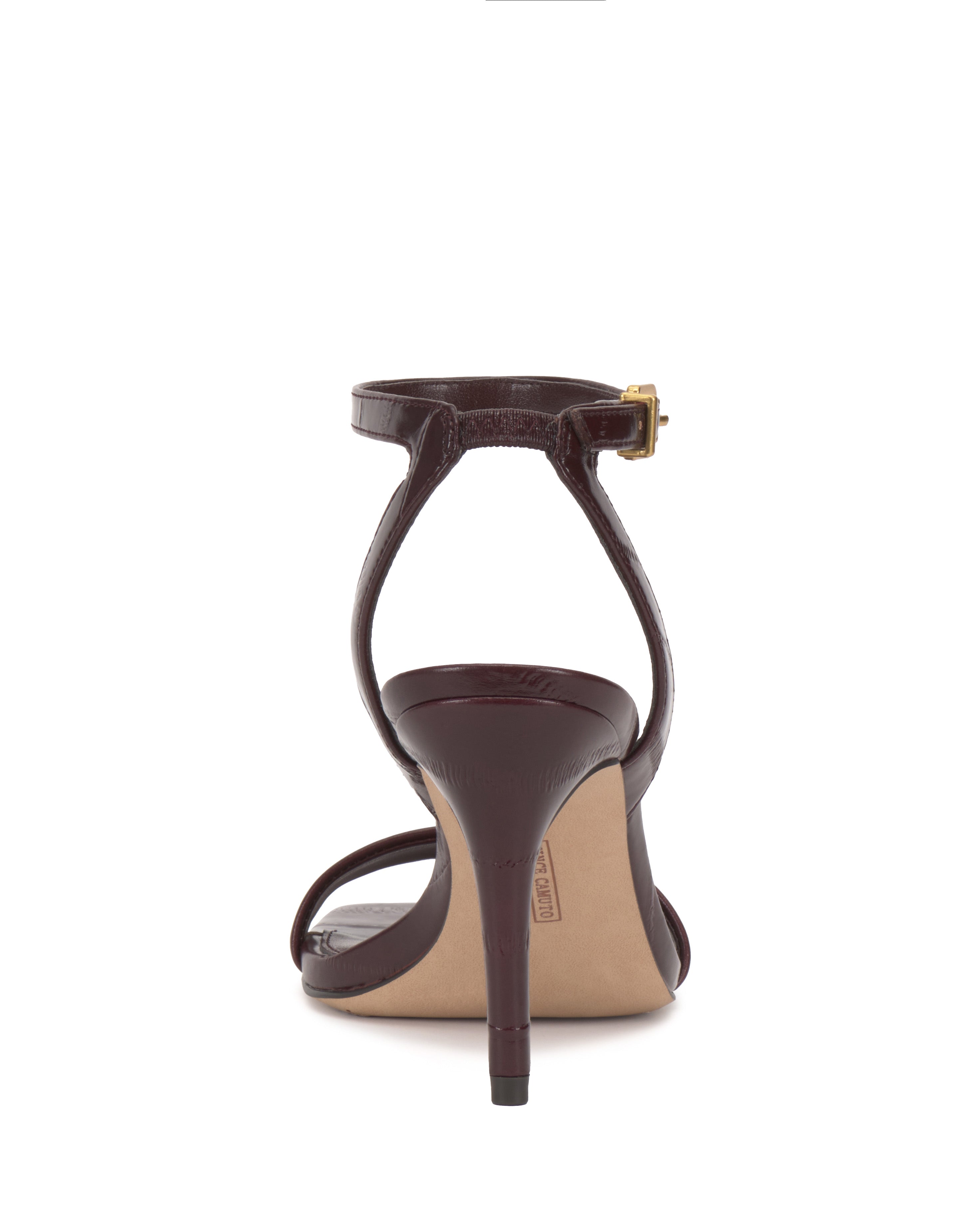 Rear view of the Vince Camuto Saprenda Sandal, a single dark brown dress sandal with an ankle strap and gold buckle, made from sleek metallic leather and set against a white background.