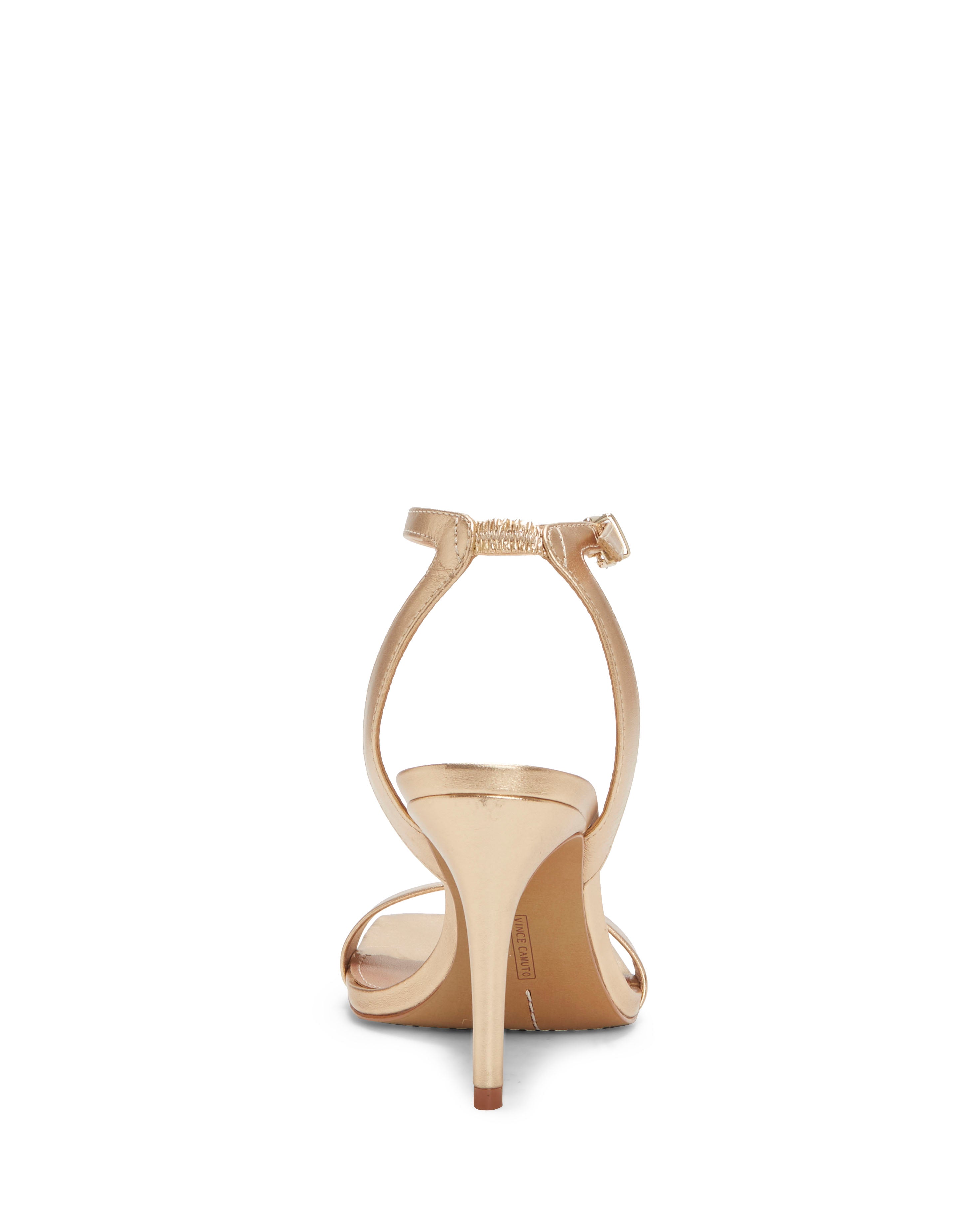 The Vince Camuto Saprenda Sandal, shown from the back against a white background, is a gold open-toe dress sandal with a slim high heel, ankle strap and buckle, and a sleek minimalist design.