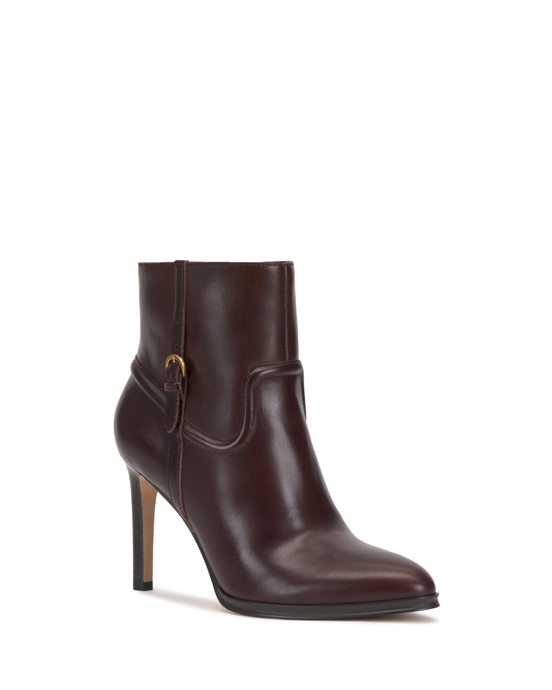 The Setily Bootie by Vince Camuto is a dark brown leather ankle boot featuring a high stiletto heel, almond toe, and a decorative strap with a small gold buckle on the side, displayed on a white background.