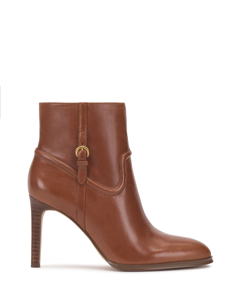 The Vince Camuto Setily Bootie is a brown leather ankle boot featuring a high, stacked heel, rounded toe, and a small gold buckle detail on the side, shown against a white background.