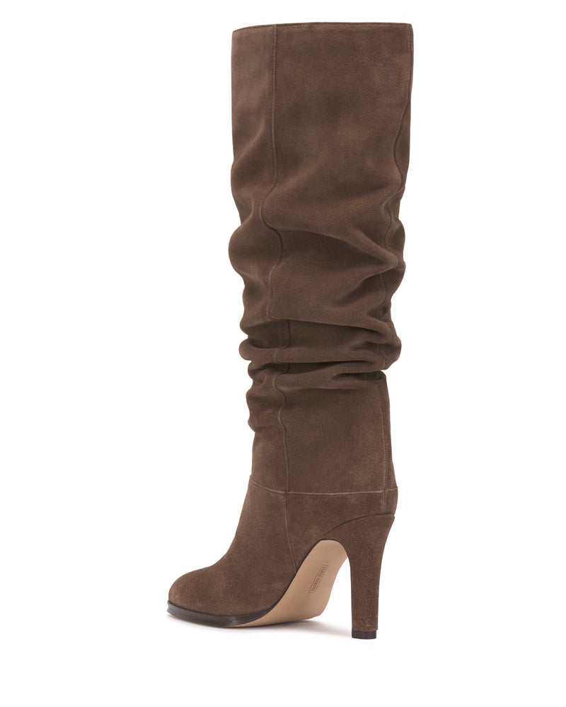 The Sorina Wide Calf Knee High Boot by Vince Camuto features a brown suede finish, a high heel, and a slouchy, relaxed shaft. Shown in profile against a white background, this on-trend boot seamlessly combines style and comfort—ideal for those seeking fashionable slouchy boots.