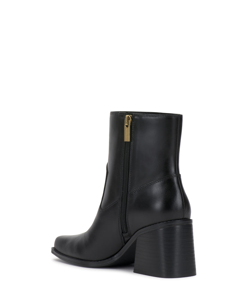 The Sybren Bootie by Vince Camuto is a black leather ankle bootie featuring a chunky block heel, pointed toe, and a gold side zipper, showcased from a rear side angle against a white background—an expression of modern sophistication.