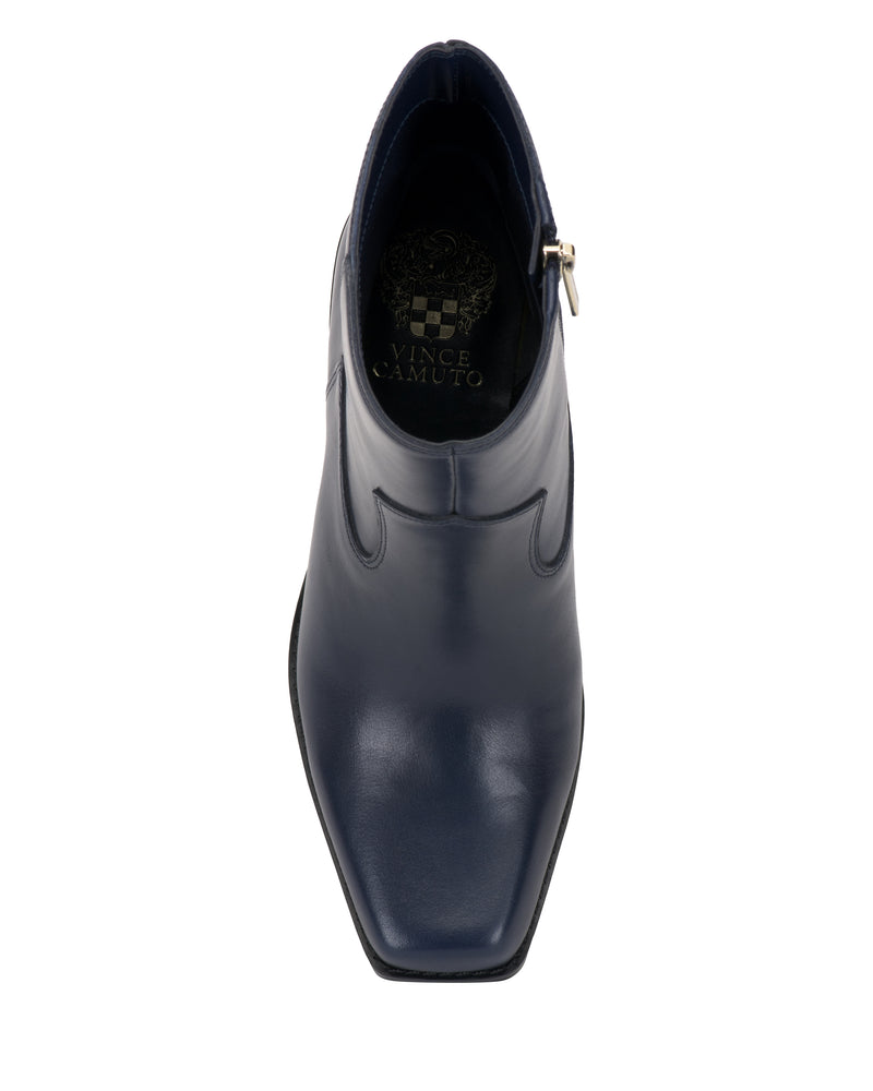 Top view of the Vince Camuto Sybren Bootie, a single dark blue leather dress shoe with a pointed toe, visible stitching, and a faint brand logo on the insole; its structured silhouette evokes a western-inspired design.