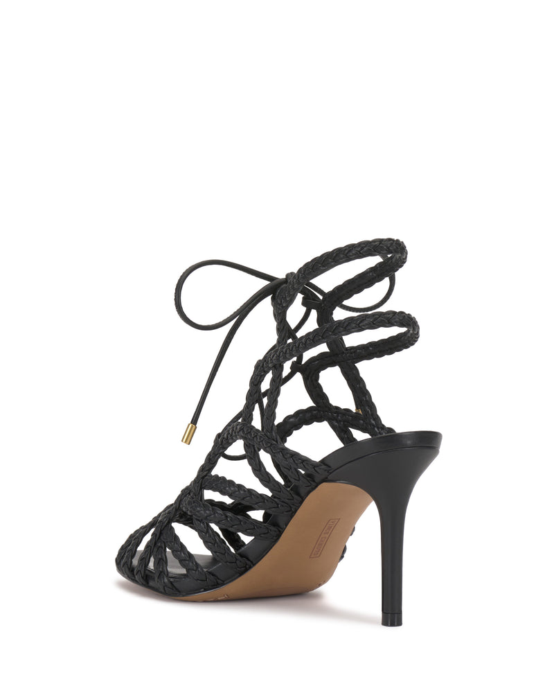 The Vince Camuto Tilly Sandal is a black woven strappy sandal with braided straps and a lace-up ankle tie, shown from the back to highlight its stiletto heel and part of the sole.