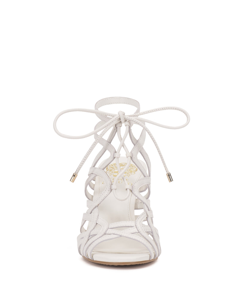 Front view of the Vince Camuto Tilly Sandal in white, showcasing a stiletto heel, intricate crisscross straps, and an ankle-tied bow, set against a plain white background.