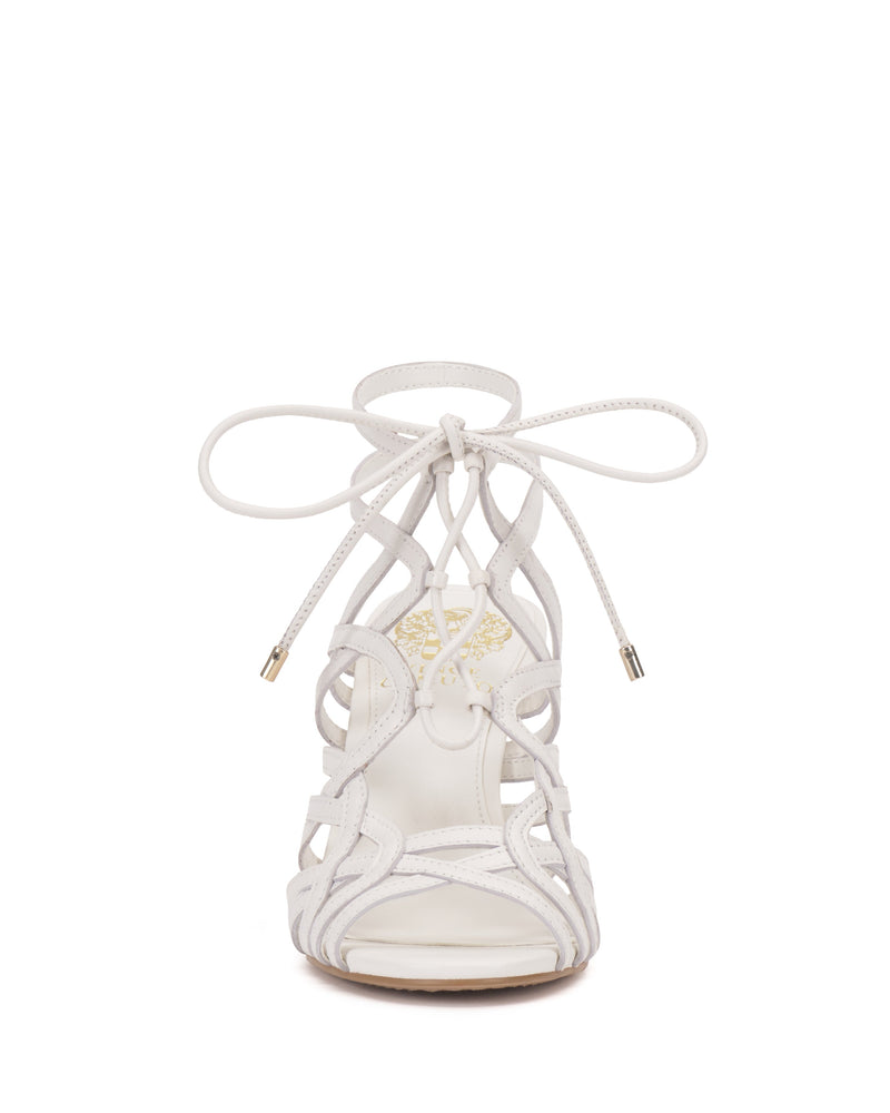 Front view of the Tilly Sandal by Vince Camuto, a white strappy stiletto with crisscross straps, lace-up design with metal tips, and decorative cutout accents.