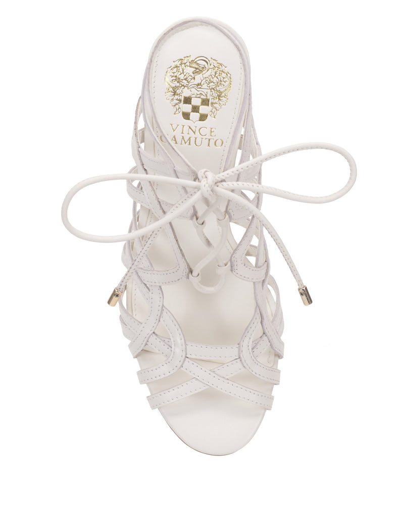 The Vince Camuto Tilly Sandal features a white strappy lace-up design with gold-toned aglets, an elegant stiletto heel, and a branded insole with the Vince Camuto logo and crest, viewed from above.