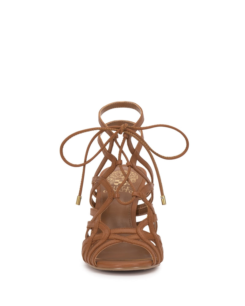 Front view of the Vince Camuto Tilly Sandal, a brown strappy stiletto with an intricate lace-up design and gold-tipped laces, shown against a white background.