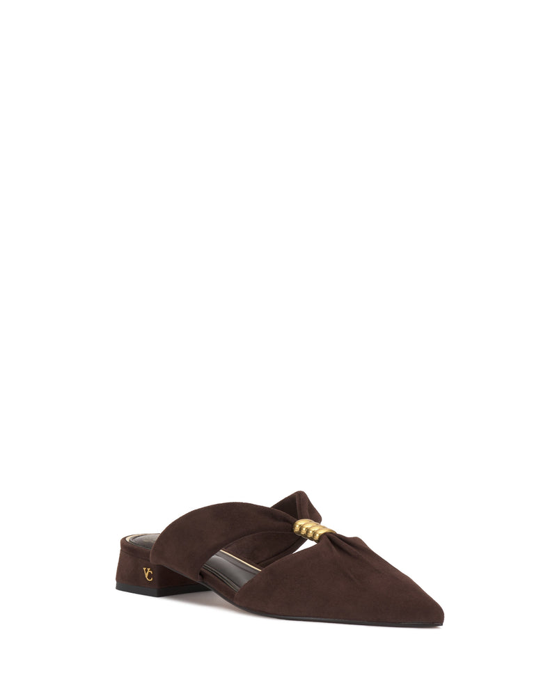 The Vince Camuto Vanika Mule is a dark brown suede shoe with a low block heel, pointed toe, gold decorative accent on top, and a subtle gold logo on the heel.