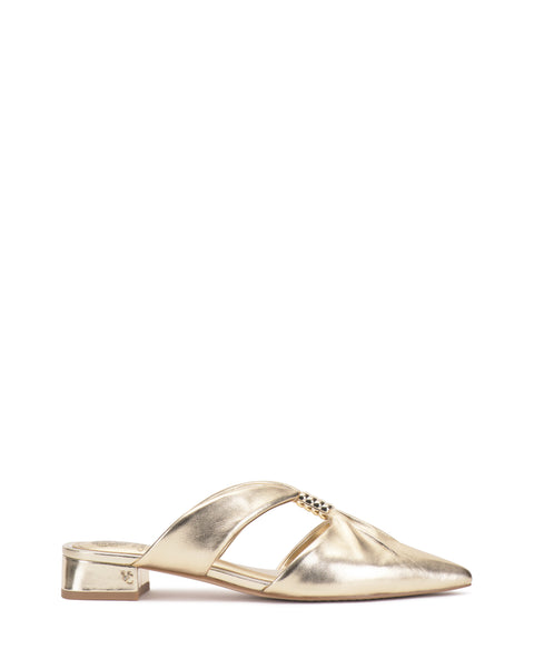 The Vince Camuto Vanika Mule is a gold metallic shoe with a low block heel, open sides, pointed toe, twisted upper detailing, and a central embellishment. Shown on a plain white background.