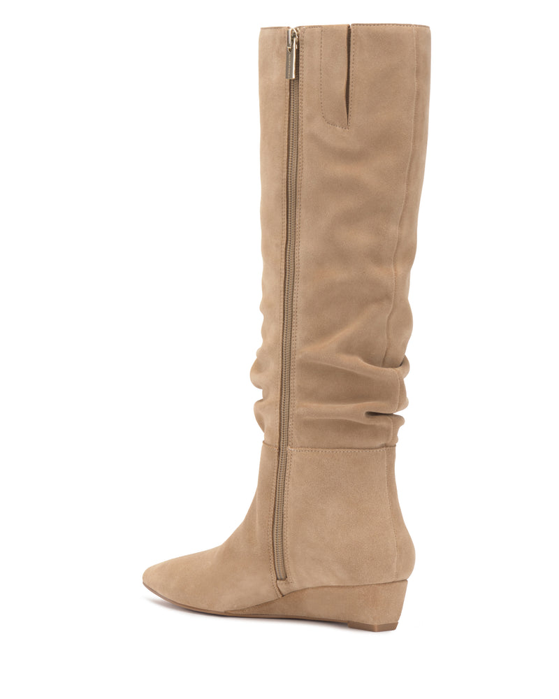 Side view of the Vince Camuto Vanisa Narrow Calf Knee High Boot, featuring tall tan suede construction, a pointed toe, visible zipper, slightly slouched shaft, low wedge heel, and smooth finish.