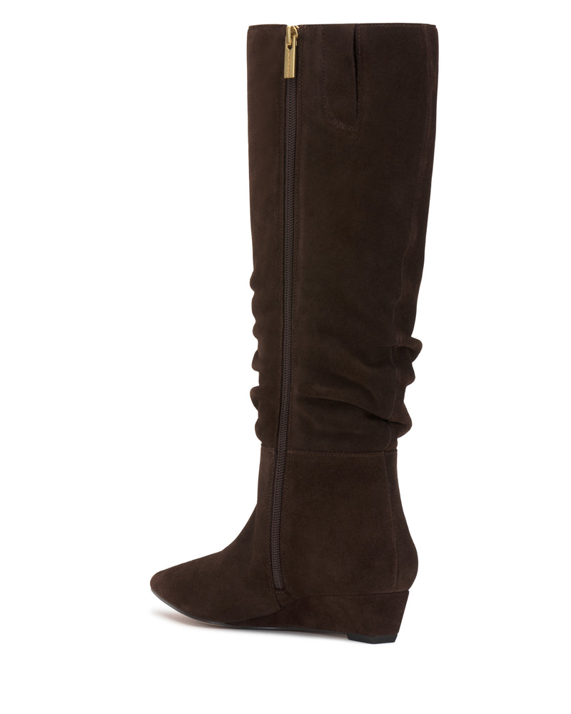 The Vanisa Wide Calf Knee High Boot by Vince Camuto is a tall, dark brown suede boot featuring a low wedge heel, side zipper, and slightly slouched shaft. The boot is displayed in side profile against a white background.