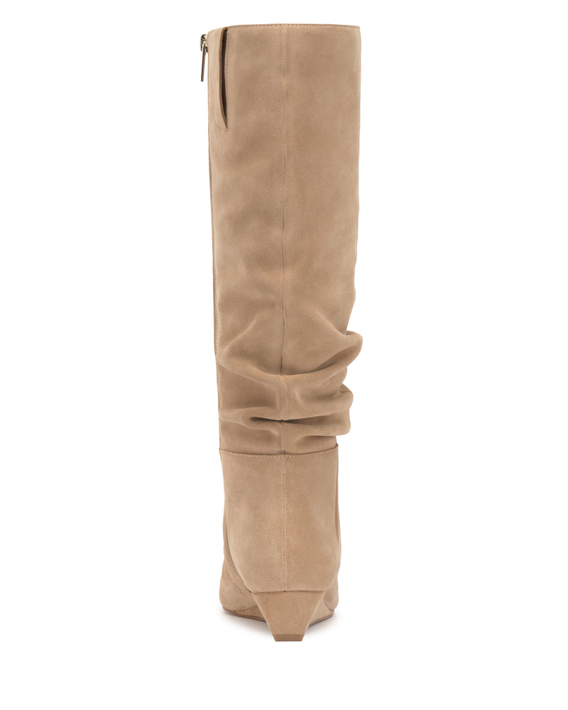The Vanisa Wide Calf Knee High Boot by Vince Camuto is shown from the back in beige suede, featuring a slouchy shaft, pointed toe, visible vertical seam up the back, and a low triangular heel.
