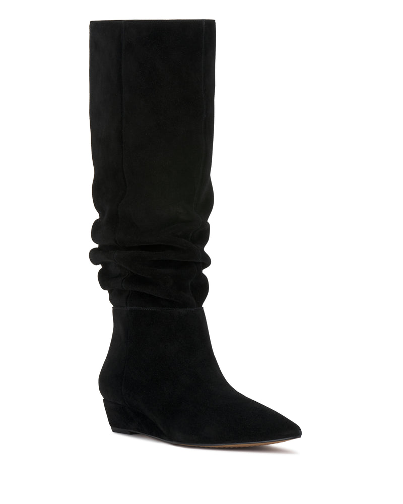 The Vanisa Knee High Boot by Vince Camuto features black suede, a pointed toe, low wedge heel, and a slouchy, relaxed shaft. Displayed on a white background, the boot is angled slightly to the right.