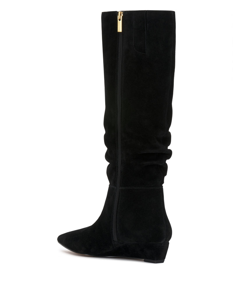 The Vanisa Knee High Boot by Vince Camuto is a black suede knee-high boot featuring a slightly pointed toe, low wedge heel, and a gold zipper at the top. Its subtle slouchy design and smooth texture are highlighted in the photo against a white background.