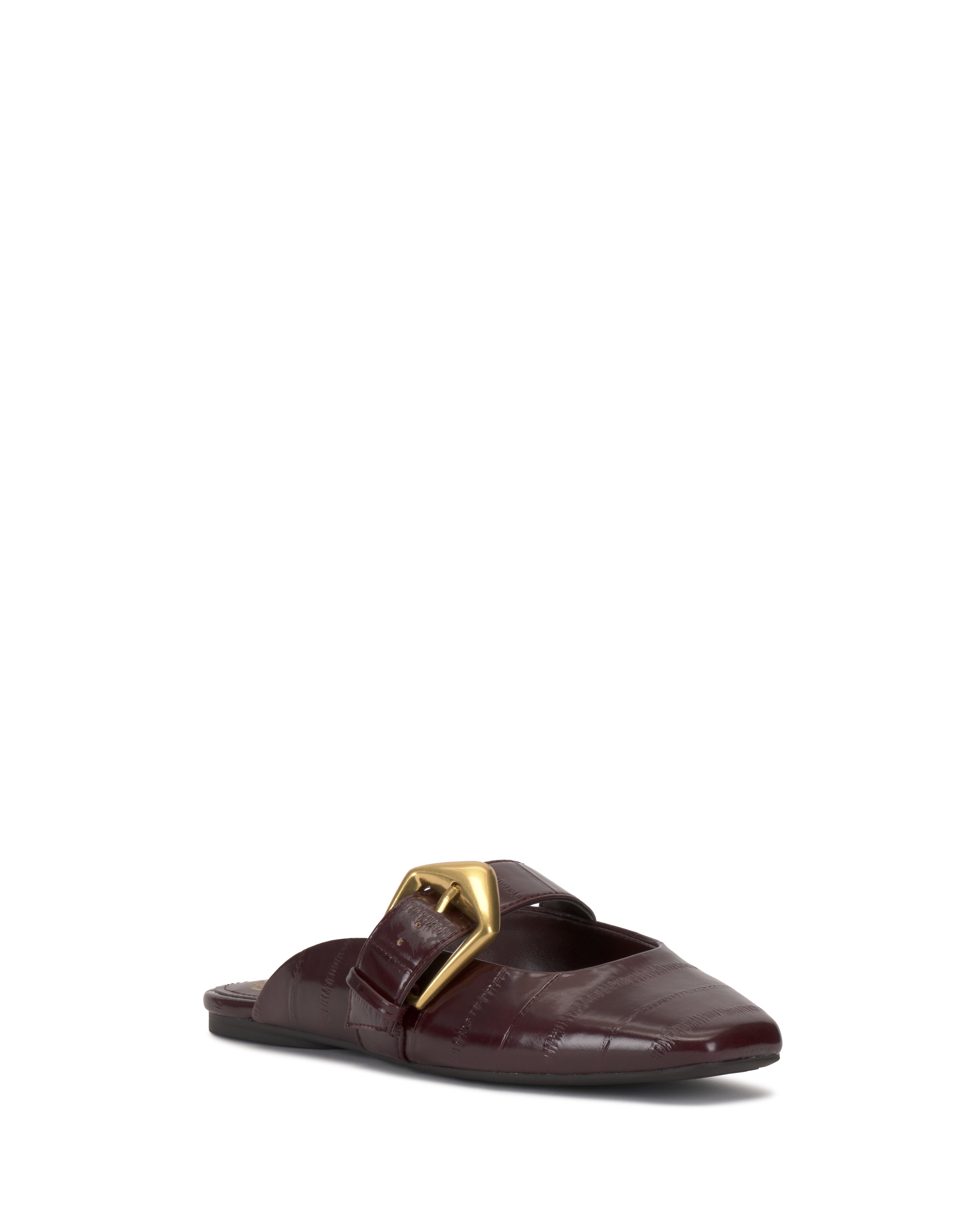 The Vellma Buckle Mule by Vince Camuto is a single burgundy flat mule with a pointed toe, textured leather finish, and a large gold buckle on the upper, shown against a white background.