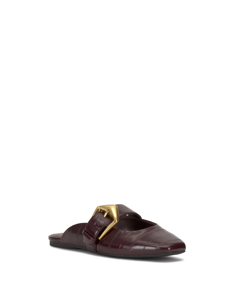 The Vellma Buckle Mule by Vince Camuto is a single burgundy flat mule with a pointed toe, textured leather finish, and a large gold buckle on the upper, shown against a white background.