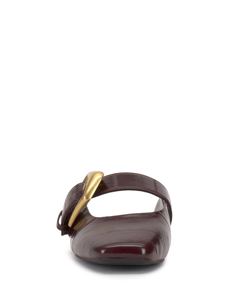 Front view of the Vince Camuto Vellma Buckle Mule in maroon leather, featuring an open toe, wide strap with a large gold buckle on the left, flat sole, and a sleek glossy finish.