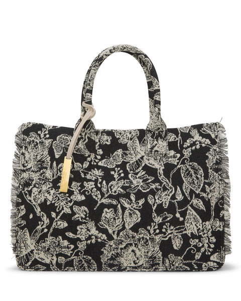 The Vince Camuto Zhury Tote Bag features a black design with white floral patterns, dual handles, fringed edges, and a gold tag accent.