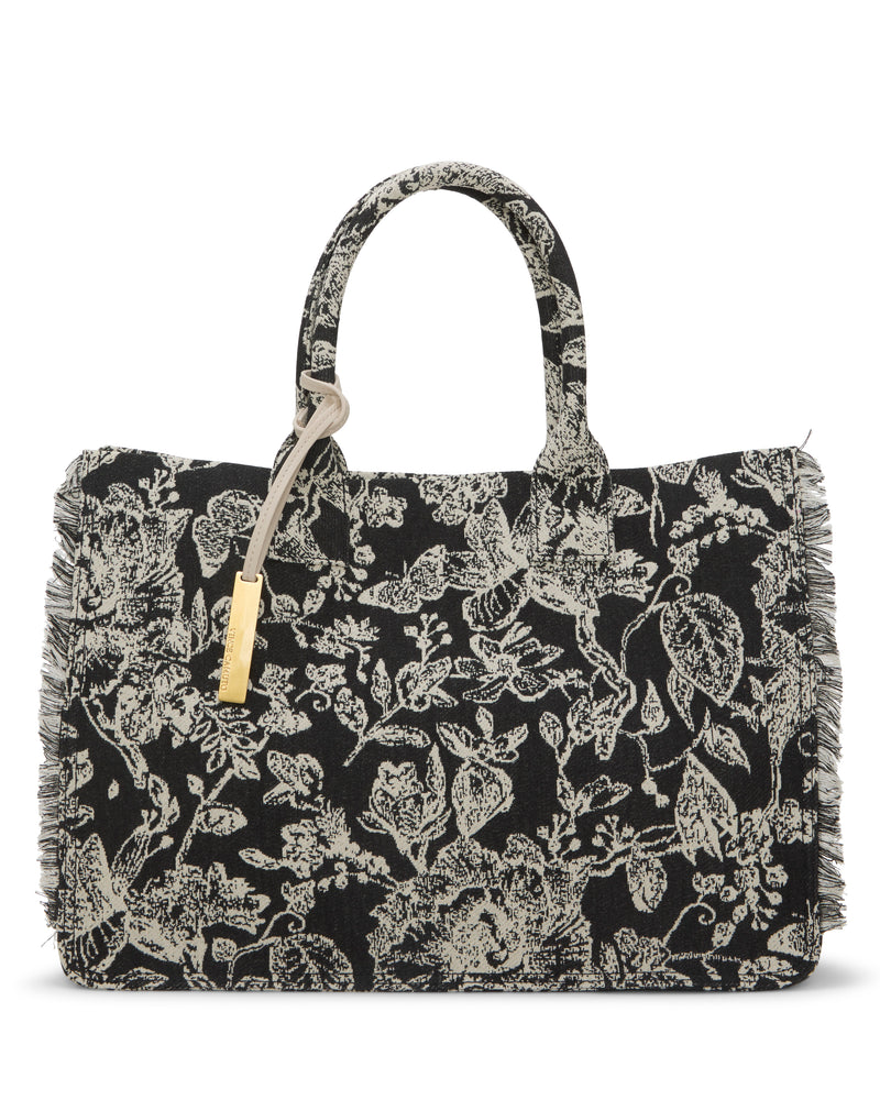 The Vince Camuto Zhury Tote Bag features a black design with white floral patterns, dual handles, fringed edges, and a gold tag accent.