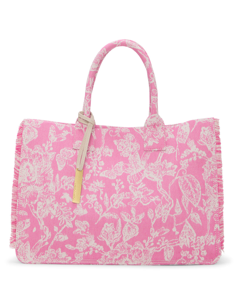 The Zhury Tote Bag by Vince Camuto is a pink tote with two handles, white floral and bird patterns, fringed edges, and a gold-tone rectangular tag for a stylish finish.