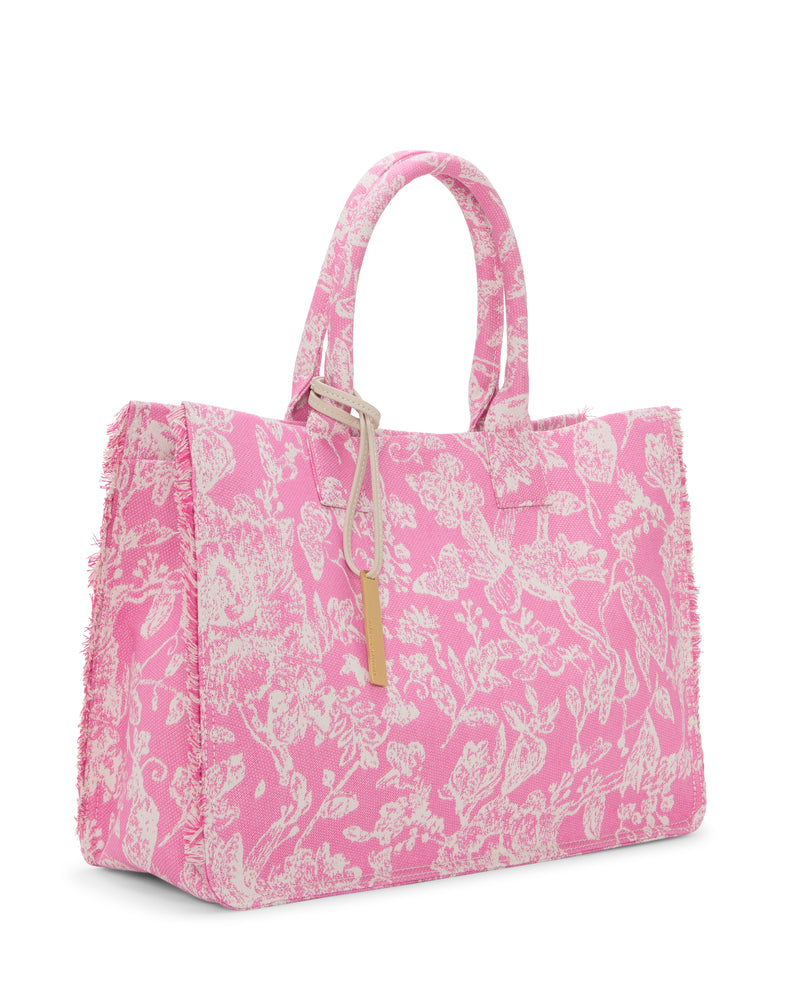 The Zhury Tote Bag by Vince Camuto showcases a pink design with white florals, two short handles, a gold rectangular tag, and textured, slightly frayed edges for extra charm.