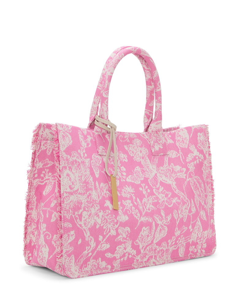 The Vince Camuto Zhury Tote Bag features a pink design with white floral and animal patterns, frayed edges, dual handles, and a gold rectangular tag that accents its soft, textured fabric appearance.